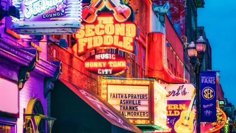 	lit neon signs for bars and clubs hanging from the business fronts in Nashville