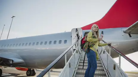 Senior woman standing on the air-stair of a plane with her boarding pass and has turned round to give one last look