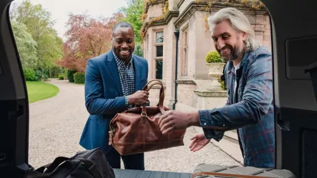 Two men retrieving luggage from boot of car whilst smiling 