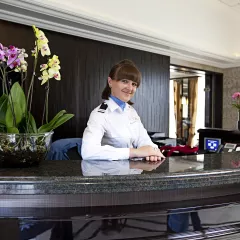 Internal shot of woman in uniform politely smiling behind a glossy, black reception desk inside the William Shakespeare cruise ship