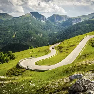 Alpina road at summer-Nockalmstrasse, curving along the natural lines of a green valley, the background showcasing nearby mountain 