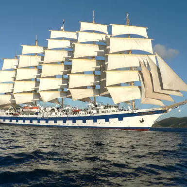 Exterior side shot of the white and blue Royal Clipper ship with tall sails cruising the ocean