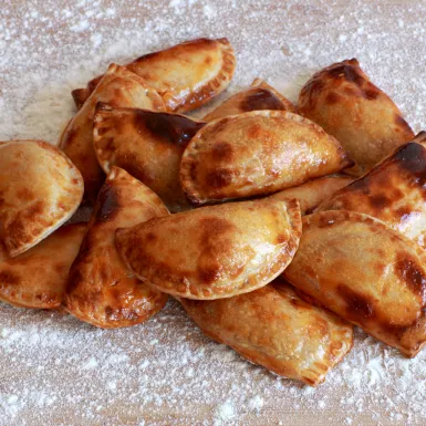 Close-up of an empanada, a turnover lightly dusted with icing sugar.