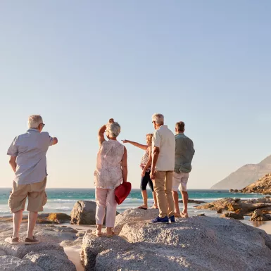 Rear view of senior friends standing on rocks looking out towards the sea