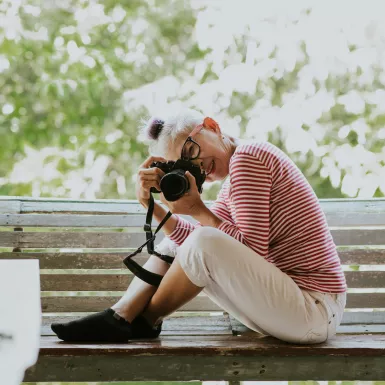 Senior Thai woman taking a professional photograph whilst sitting on a bench