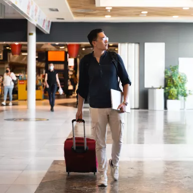 Man walking through an airport with his laptop and suitcase