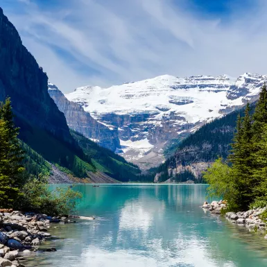 Beautiful Lake Louise with Victoria Glacier in the background and a glistening emerald lake. Several canoes can be seen at a distance on the lake.