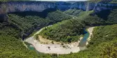 Curving Ardeche River, surrounded by tall trees and a cliff, France