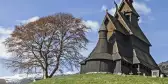 Preserved wooden Hopperstad Stave Church besides a tree atop a green hill, Norway