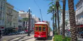 Red New Orleans Streetcar in motion along the downtown line along tall palm trees and street sidewalks