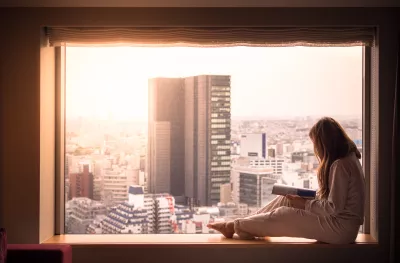 A woman in her pyjamas, looking out of her hotel window at the cityscape of Shibuya, Tokyo. 