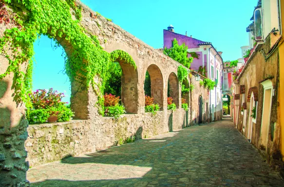 Old stone wall with arches and flowers on old European street, Italy