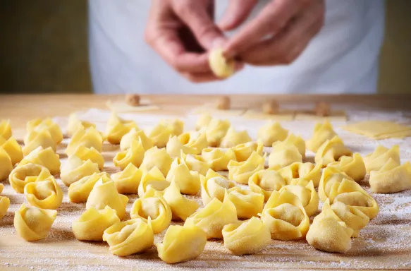 A man making homemade tortellini, on a flour coated wooden table.