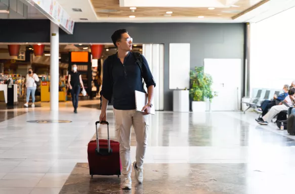 Man walking through an airport with his laptop and suitcase