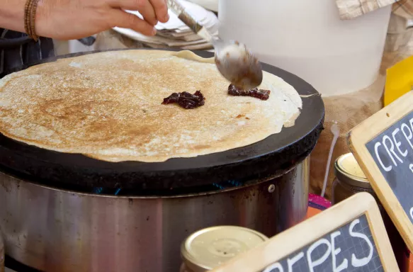 Crepes cooking in open air market being topped with chocolate by a spoon