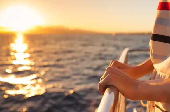 Close-up of hands holding onto rail on a yacht during sunset