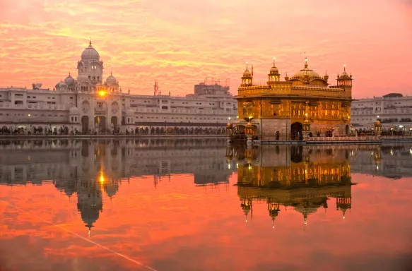 Golden Temple in Amritsar, Punjab, India. Orange sunset and buildings reflecting on water in front.