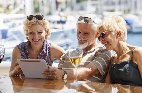 Senior friends smiling and using a digital tablet on a yacht.