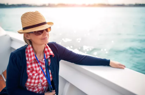 A tourist with a sunhat on a deck of a cruise ship looking at the ocean