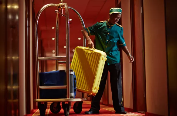 Hotel Bellboy lifting yellow suitcase from Bellhop cart