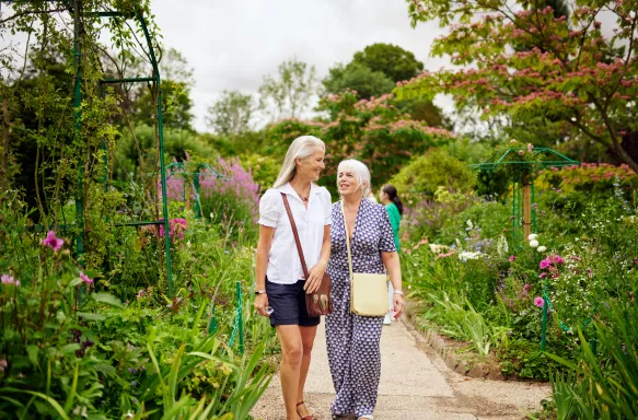 Two senior friends walking amongst flowers and greenery at a garden