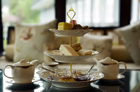 Three tier cake stand set up for an afternoon tea with cakes and servings of jam, plus two teapots