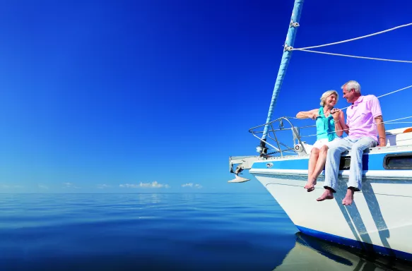 Happy senior couple sitting on the bow of a sail boat on a calm blue sea