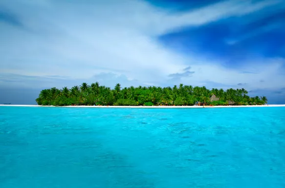 Stunningly turquoise and clear ocean waters surrounding Alimathà island with lush vegetation in the Maldives