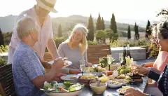 A group of mature friends are sitting around an outdoor dining table in Tuscany, Italy