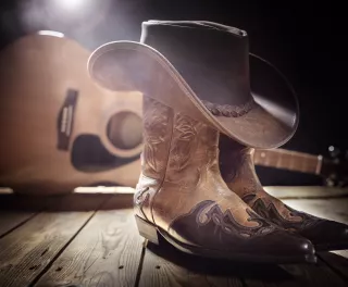 Cowboy boots with cowboy hat on top, a guitar in the background