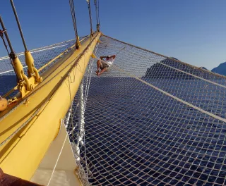 Man relaxing on the ship Bow netting in low afternoon sunlight