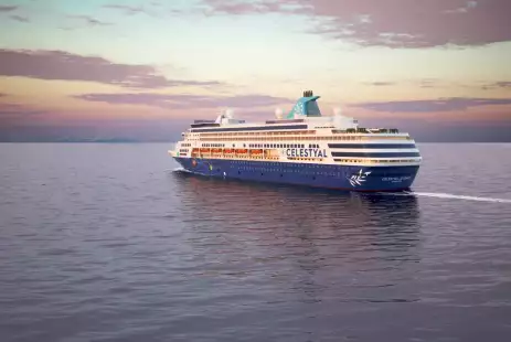 Image of the Celestyal ocean cruise ship sailing along the sea with a sunset full of pastel purples and yellow hues